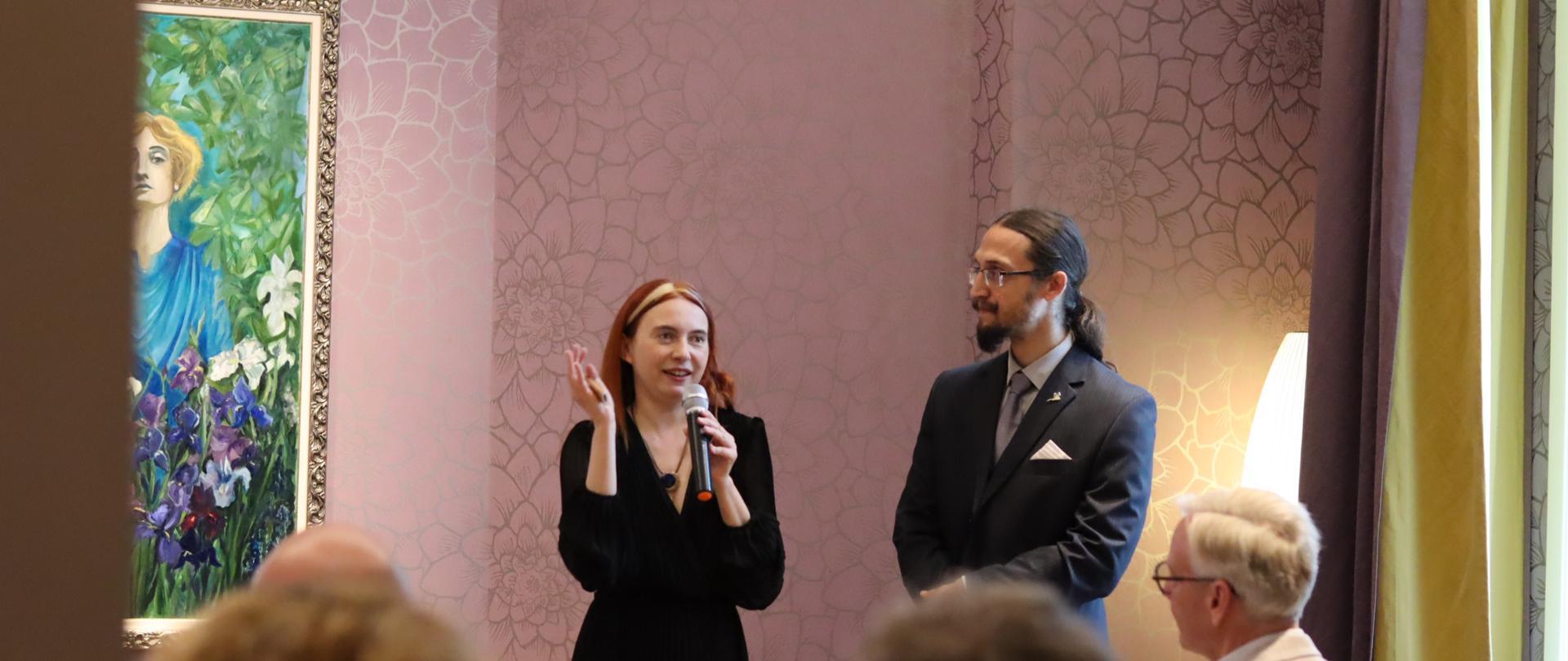 „Pasja i sztuka pomiędzy Polską a Norwegią – Dagny Juel Przybyszewska i Stanisław Przybyszewski” – spotkanie w ramach polskiego przewodnictwa w Radzie Państw Morza Bałtyckiego; Przed obrazem przedstawiającym Dagne Juel Przybyszewską w kwiatach stoi autorka Maria Molenda I Maciej Walasek przedstawiciele Fundacji Nomina Rosae