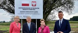 Goście uroczystości na tle tablicy informującej o dofinansowaniu ze środków budżetu państwa. 