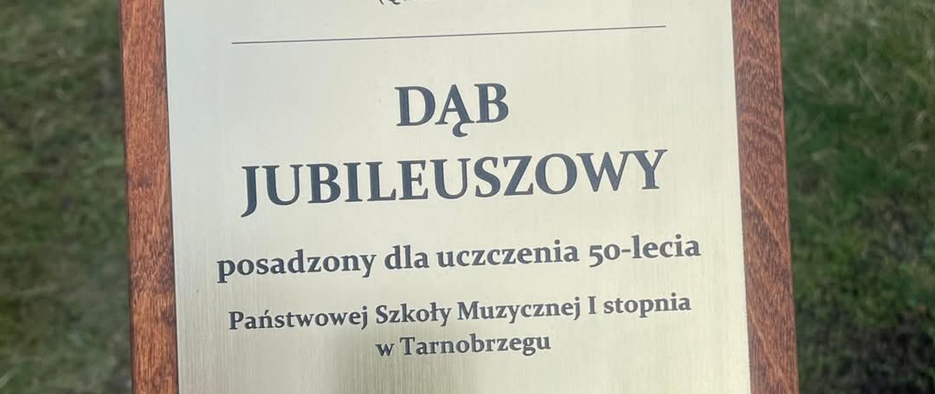 Zdjęcie przedstawia tablicę drzewa posadzonego z okazji Jubileuszu 50-lecia szkoły. Na tablicy znajduje się również cytat oraz data.