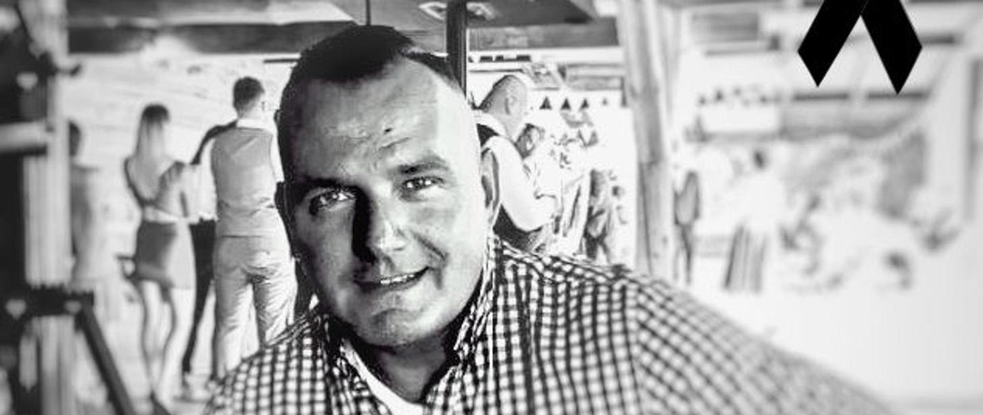 Czarno-białe zdjęcie przedstawiające mężczyznę na tle innych osób.