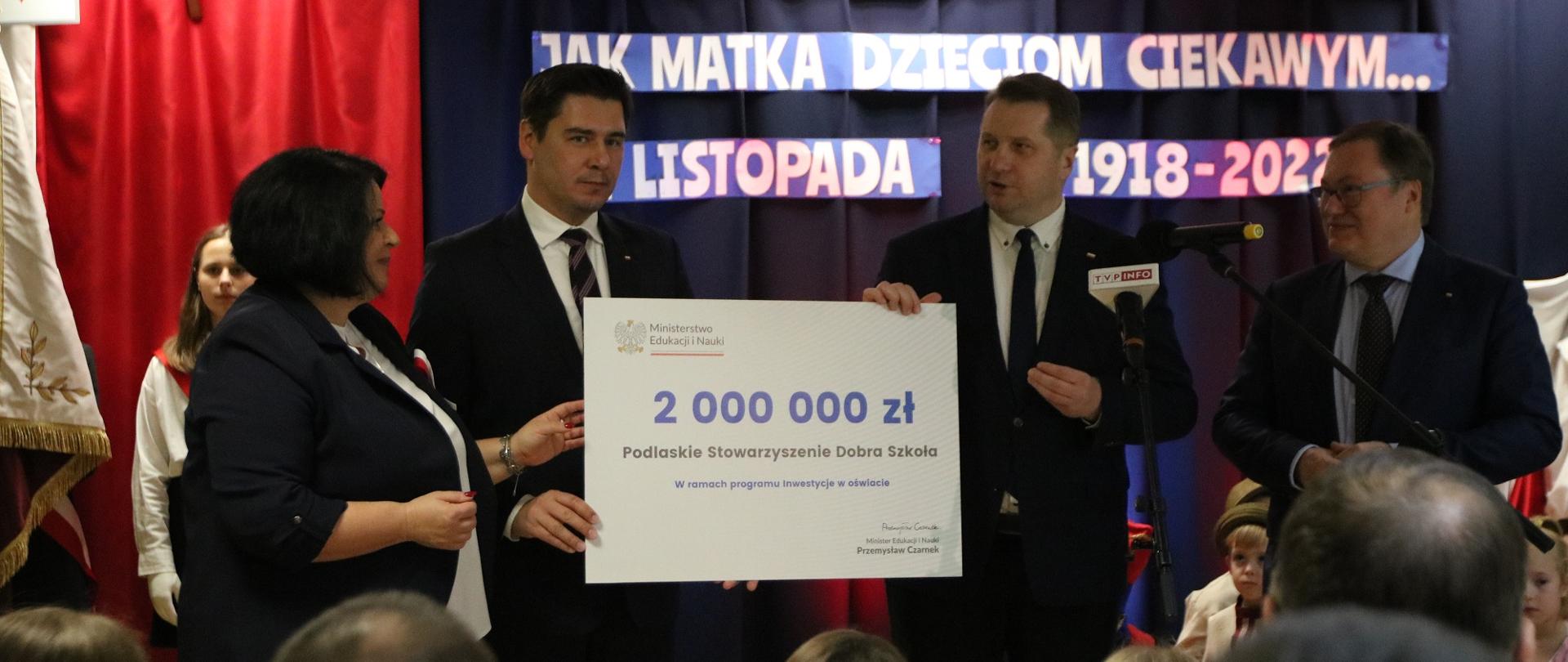 Minister Czarnek i mężczyzna w garniturze stoją na tle granatowej ściany i trzymają duży symboliczny czek z napisem 2 000 000 zł.