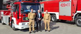 Fotografia przedstawia Lubuskiego Komendanta Wojewódzkiego PSP w Gorzowie Wlkp., Komendanta Powiatowego PSP w Strzelcach Krajeńskich oraz Burmistrza Drezdenka pozujących przed pojazdami pożarniczymi na tle Jednostki OSP Drezdenko