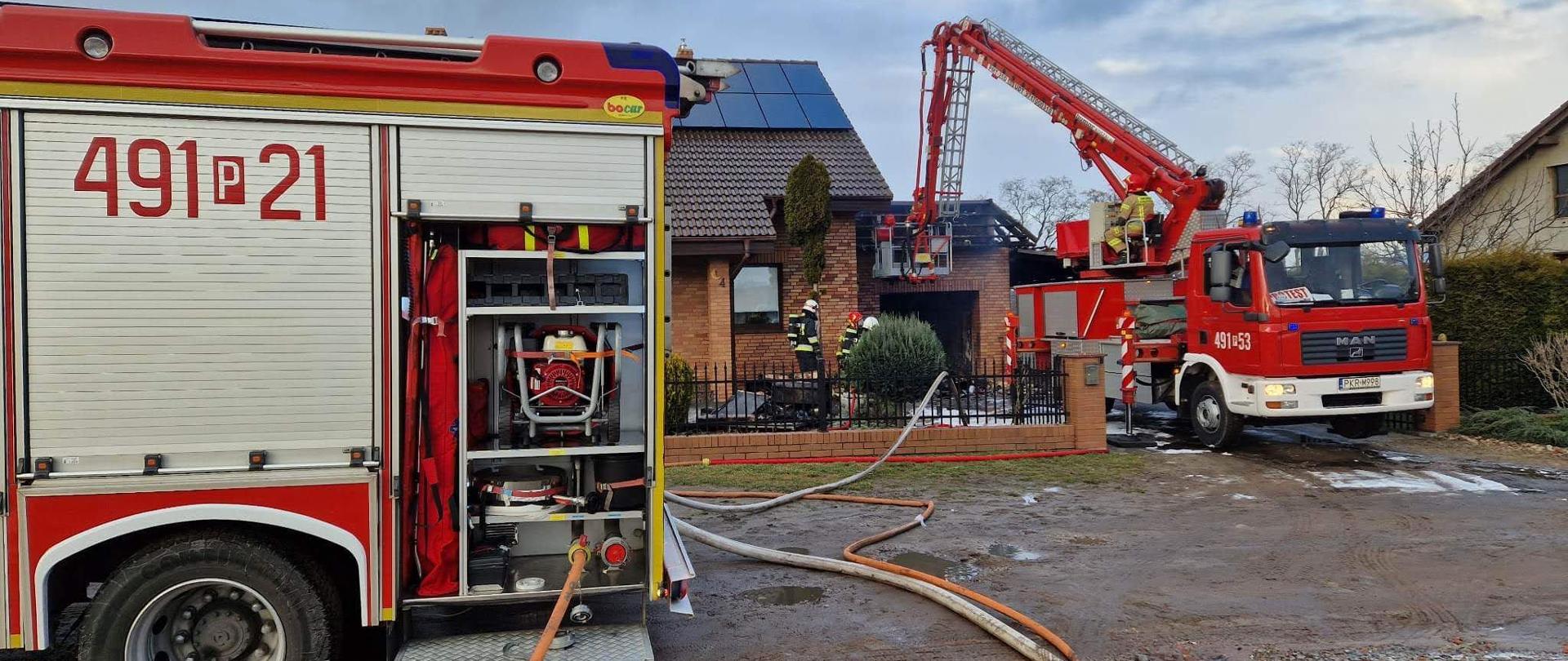 Na jezdni przed obiektem objętym działaniami znajduje sie pojazd gaśniczy oraz podnośnik hydrauliczny. Po drodze prowadzone są odcinki węży zasilające prądy gaśnicze. Strażacy z kosza podnośnika hydraulicznego dokonują oględzin więźby dachowej pod kątem występowania ukrytych zarzewi ognia. 