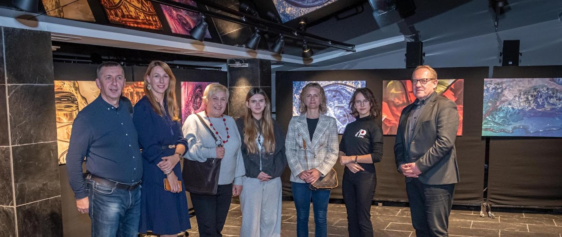 Słuchacze i nauczyciele stoją na tle wystawy