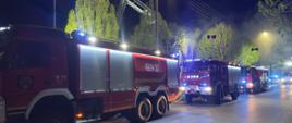 Wozy strażackie stoją przed budynkiem. Nad dachem strażacy pracują w koszu podnośnika