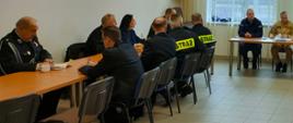 Kilkunastu strażaków siedzi przy stołach w świetlicy.