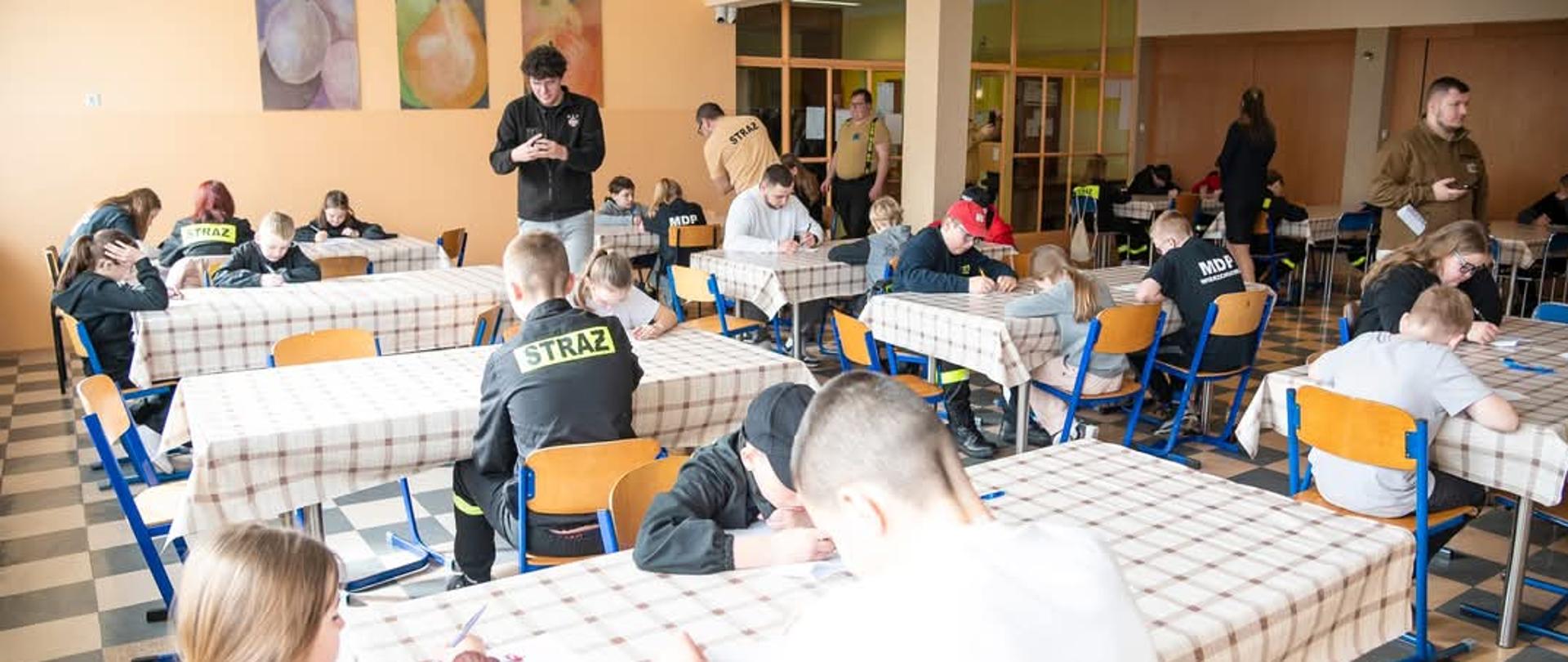 Na zdjęciu widać dzieci i młodzież, która rozwiązuje test wiedzy z zakresu pożarnictwa i pierwszej pomocy. 