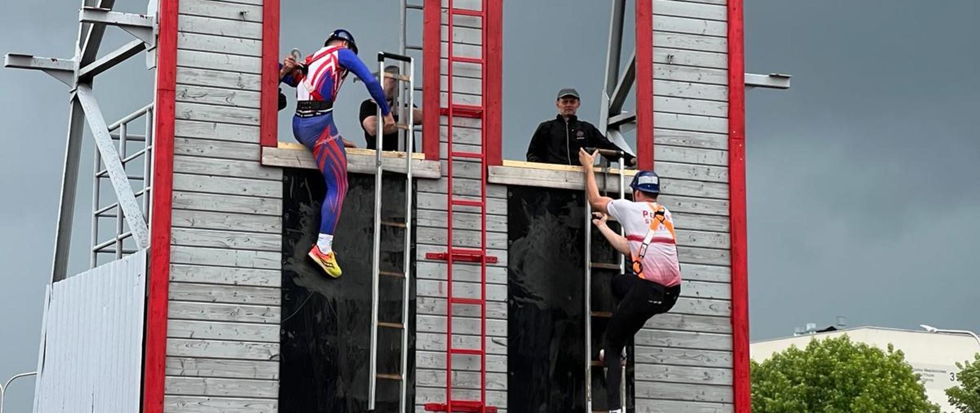 XXXII Świętokrzyski Turniej w Dwuboju Pożarniczym - zawodnicy wspinają się po ścianie z drabiną hakową