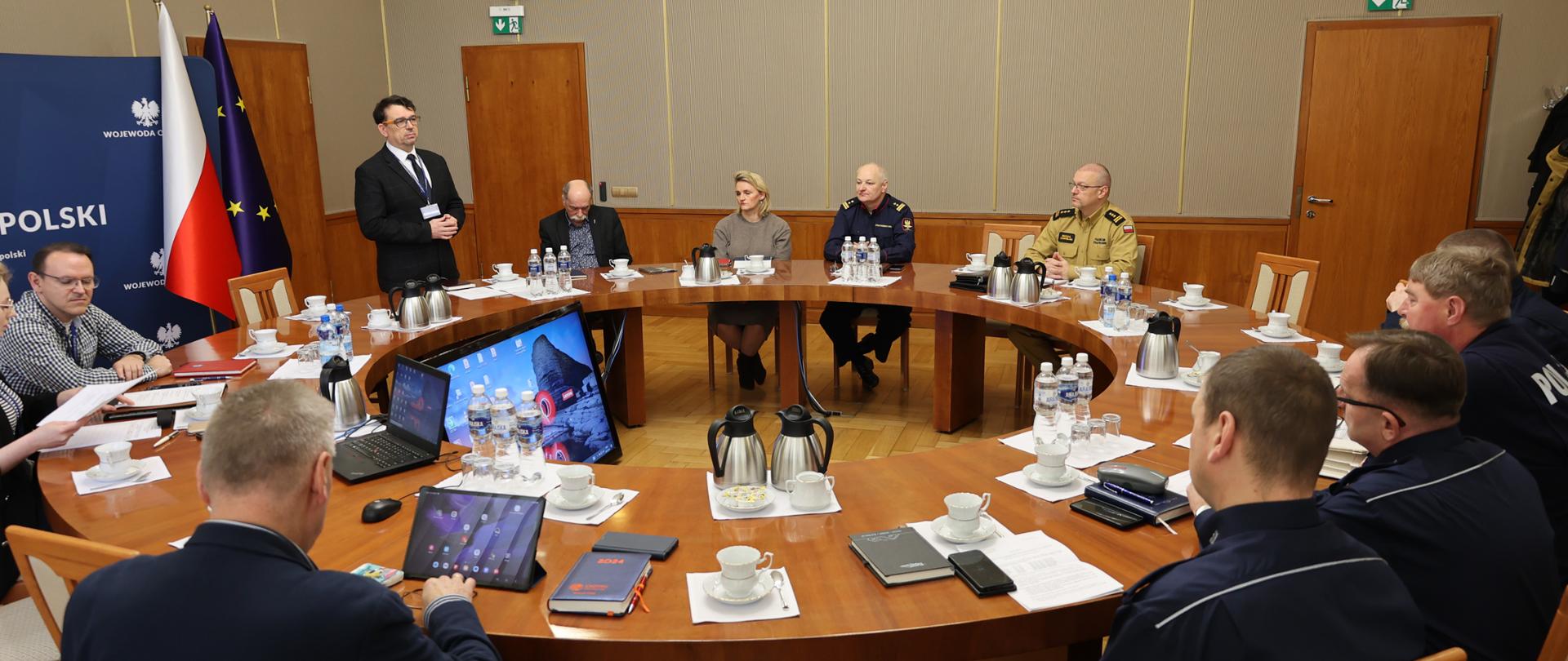 Na zdjęciu widać uczestników posiedzenia Wojewódzkiego Zespołu Interdyscyplinarnego ds. bezpieczeństwa imprez masowych. uczestnicy siedzą przy okrągłym stole. Prowadzący posiedzenia, Dyrektor Wydziału Bezpieczeństwa i Zarządzania Kryzysowego naszego Urzędu, Pan Piotr Tarapata stoi i mówi do pozostałych uczestników. 