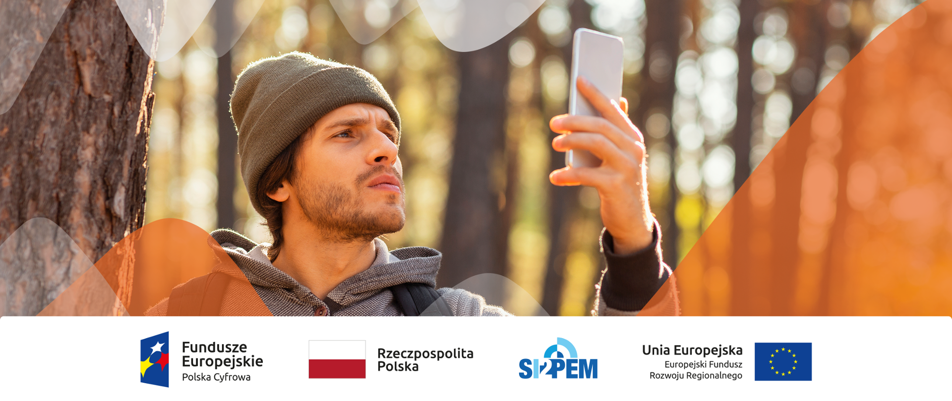 Zdjęcie - mężczyzna w lesie, do góry podnosi rękę, w której trzyma telefon komórkowy, szuka zasięgu.