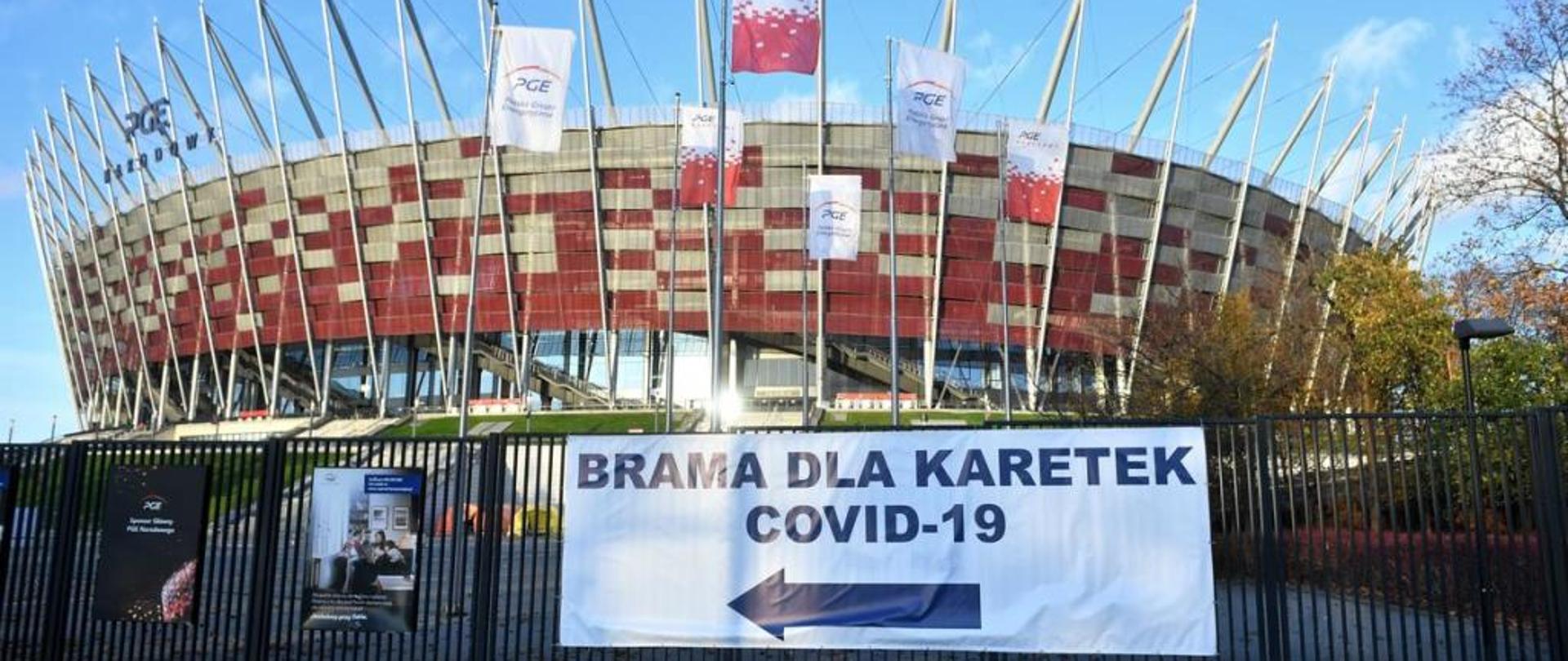 Stadion Narodowy w Warszawie, na pierwszym palnie ogrodzenie stadionu na którym znajduje się baner informujący o wjeździe dla karetek 