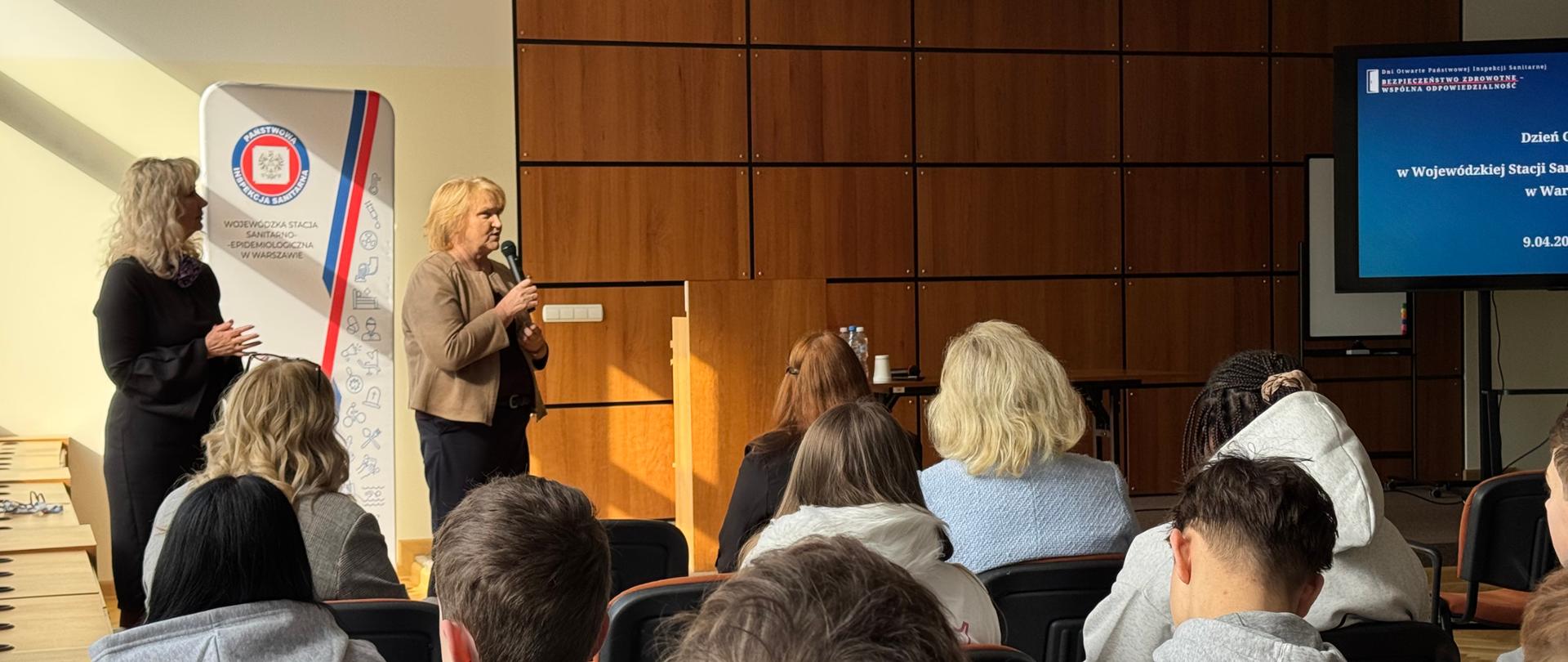 Dwie osoby prowadzące spotkanie stoją przed uczestnikami w sali konferencyjnej.