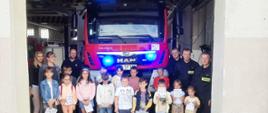 Dzieci z wizytą w Jednostce Ratowniczo – Gaśniczej w Żurominie stoją przed otwartym garażem ze strażakami