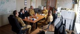 Funkcjonariusze wydziału operacyjnego siedzą przy stole podczas narady w stanowisku kierowania.