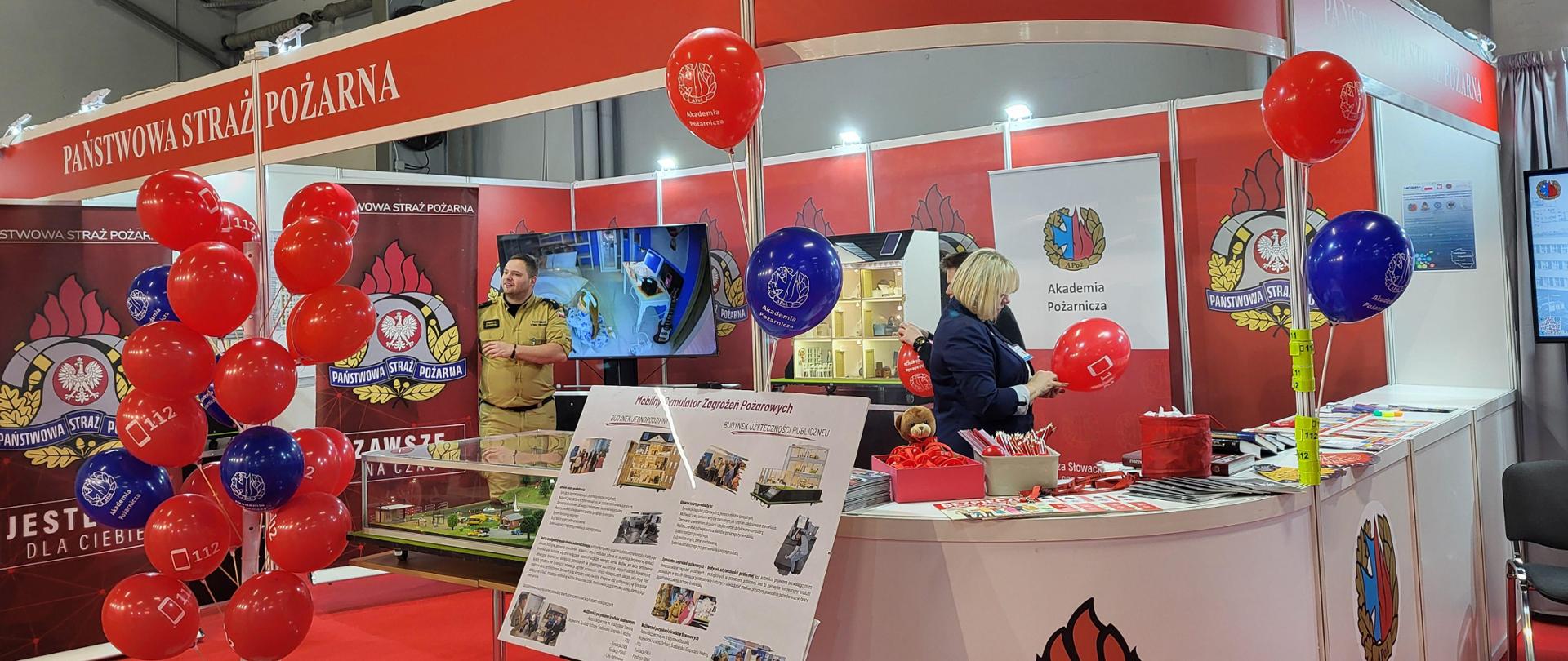 Strażak i kobieta na stoisku PSP, na którym wystawiane są materiały edukacyjne i promocyjne