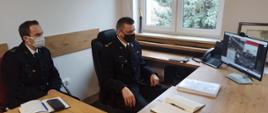 Zdjęcie przedstawia Komendanta Powiatowego PSP w Brodnicy oraz Dowódcę JRG podczas przeprowadzonej w trybie zdalnym narady rocznej kadry kierowniczej Państwowej Straży Pożarnej w województwie kujawsko-pomorskim. Komendant i Dowódca siedzący przy biurku w mundurze oglądają prezentowane materiały.