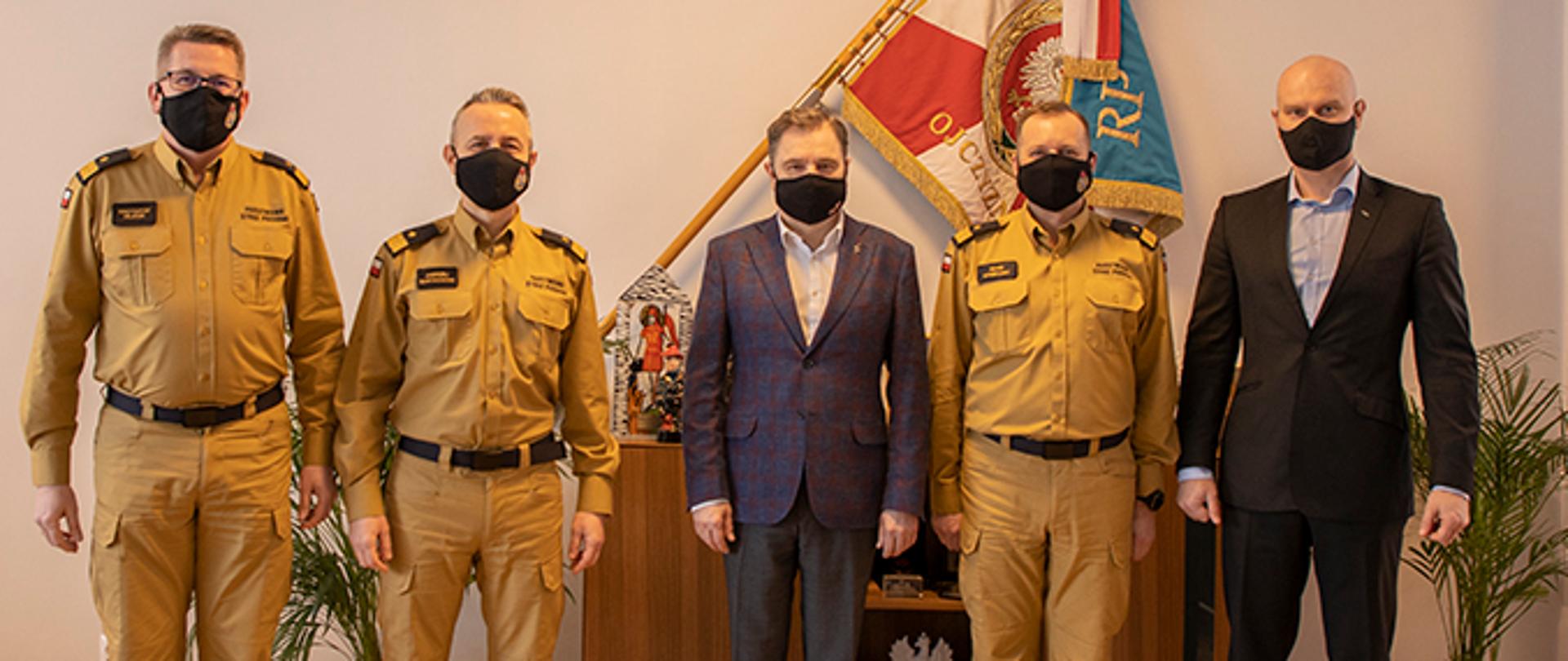 Zdjęcie pamiątkowe ze spotkania. Od lewej, w maseczkach ochronnych stoją : nadbrygadier Krzysztof Hejduk, nadbrygadier Andrzej Bartkowiak, Piotr Duda, nadbrygadier Adam Konieczny, Bartłomiej Mickiewicz. W tle wiszący na ścianie sztandar Komendy Głównej Państwowej Straży Pożarnej