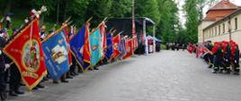 Widok z przodu. Plac apelowy podczas uroczystego wciągania flagi państwowej na maszt. Z lewej strony salutują poczty sztandarowe OSP, z prawej strony salutują proporce MDP. 