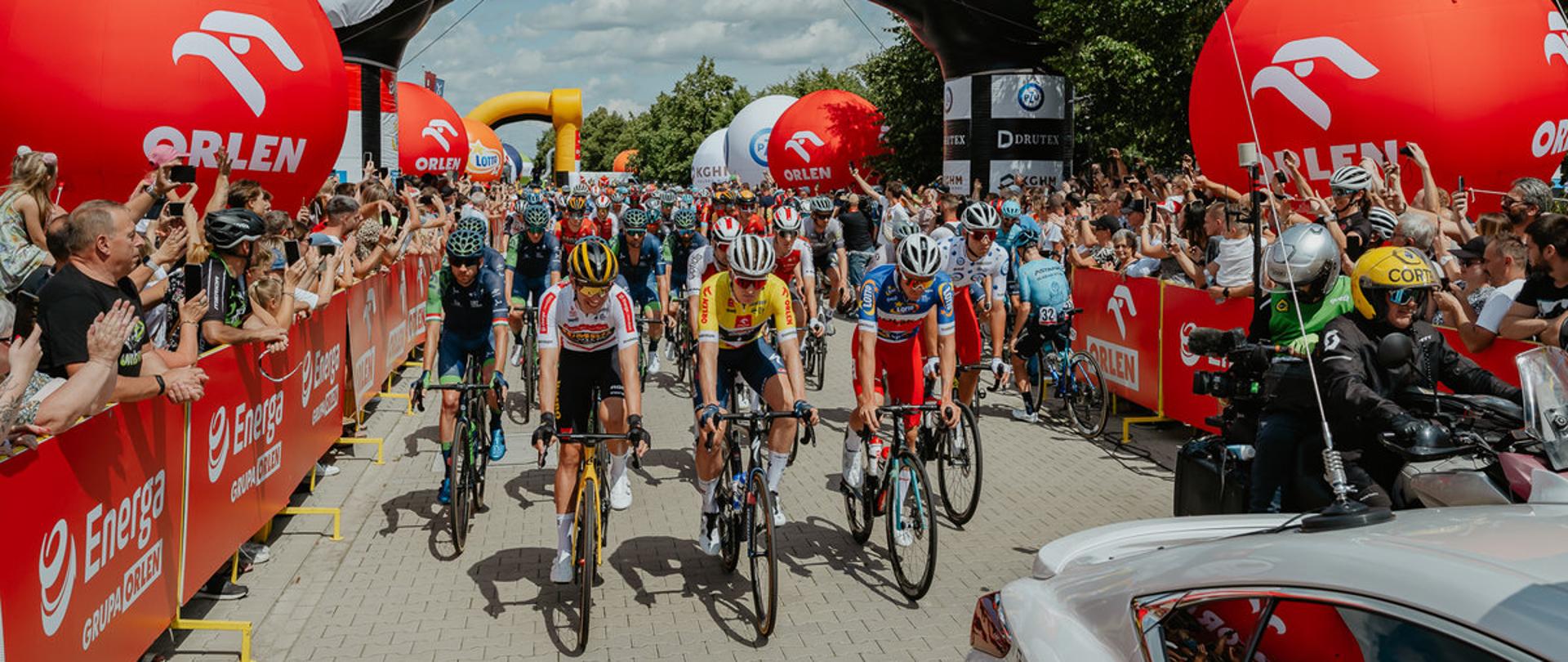 Kolarze na rowerach obok kibice.