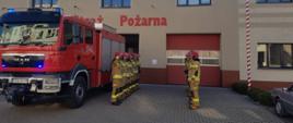 Strażacy oddali hołd kolegom z Ukrainy. Plac przed Komendą Powiatową PSP w Rawiczu. Przed budynkiem stoi wóz strażacki z włączonymi niebieskimi sygnałami błyskowymi, a obok niego strażacy z dwóch zmian służbowych. Stoją na przeciwko siebie w dwóch szeregach. Z prawej strony biało-czerwony maszt, na którym powiewa flaga narodowa.