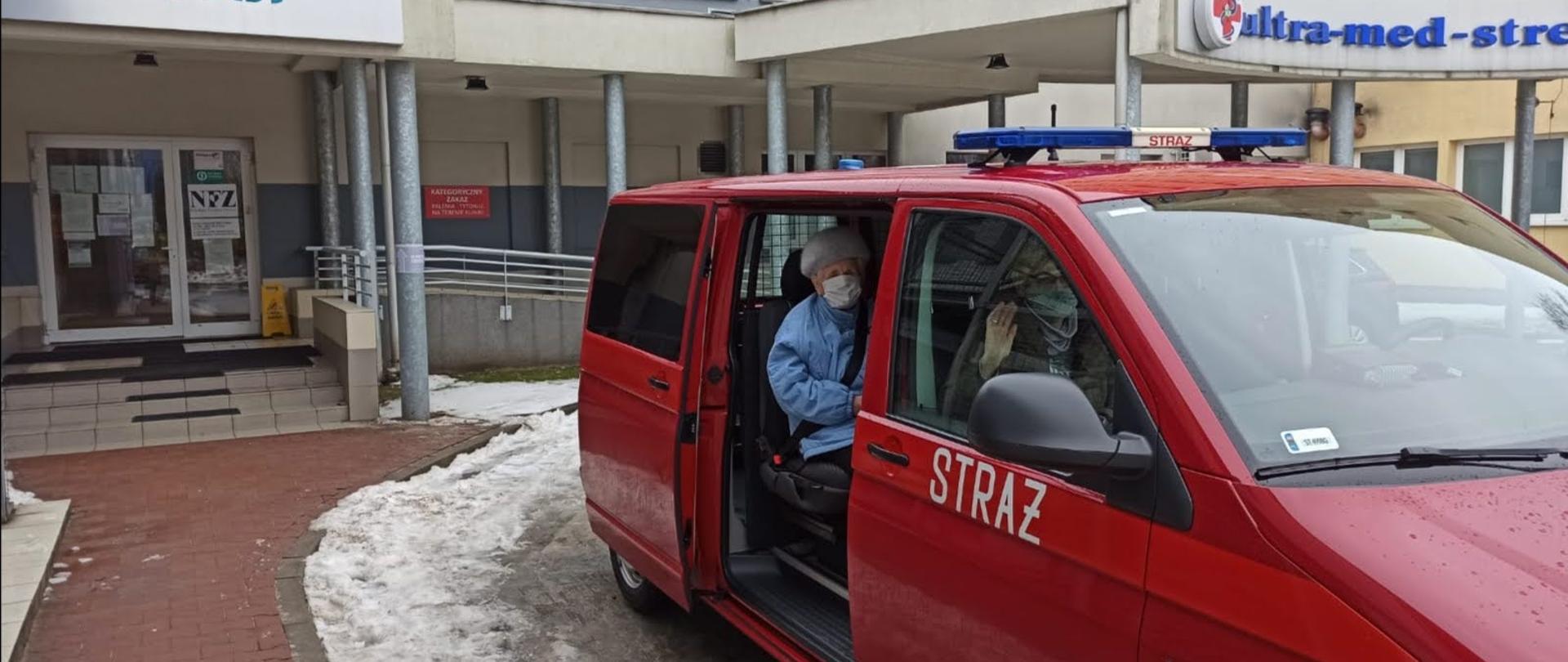 Dwie starsze Panie siedzące w samochodzie strażackim lekkim kwatermistrzowskim na tle ośrodka zdrowia