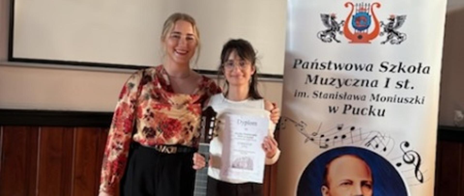 nauczycielka z uczennicą, która trzyma dyplom i gitarę
