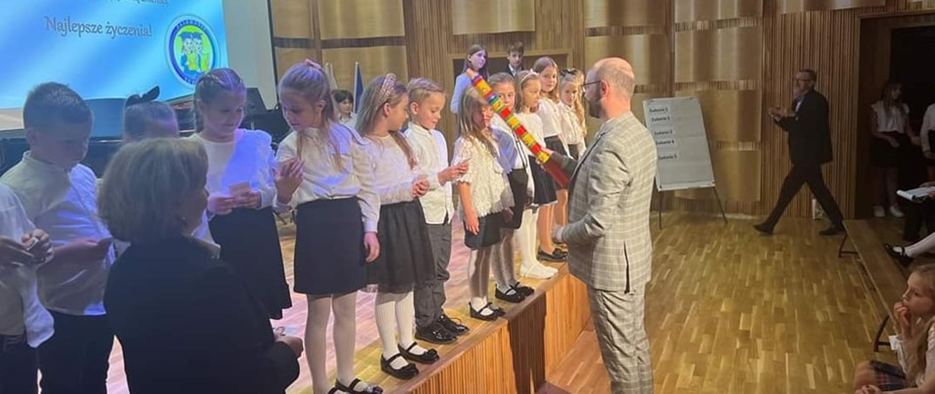 Zdjęcie sali koncertowej w której dyrektor pasuje dzieci na uczniów szkoły.