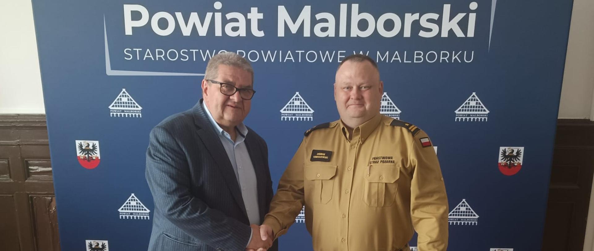 Starosta i komendant straży pożarnej ściskają sobie dłoń podczas przekazania fantomu wraz z oprzyrządowaniem do prowadzenia szkoleń z zakresu ratownictwa medycznego