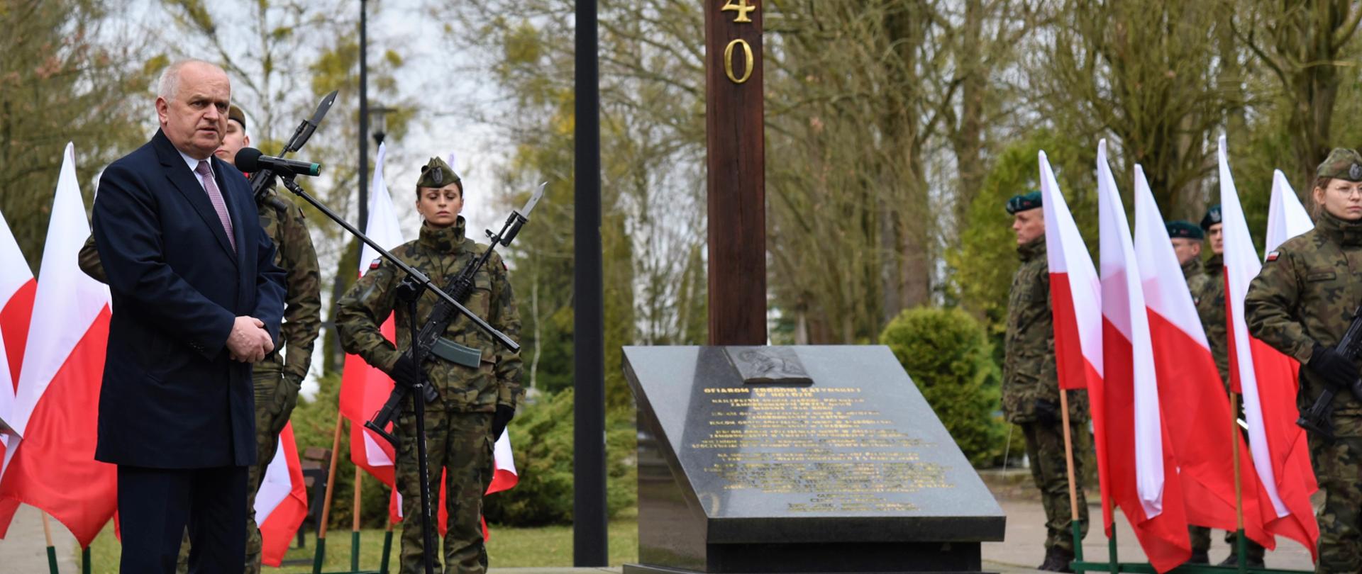 Wojewoda przemawia w czasie uroczystości na cmentarzu, w tle krzyż z napisem Katyń 1940