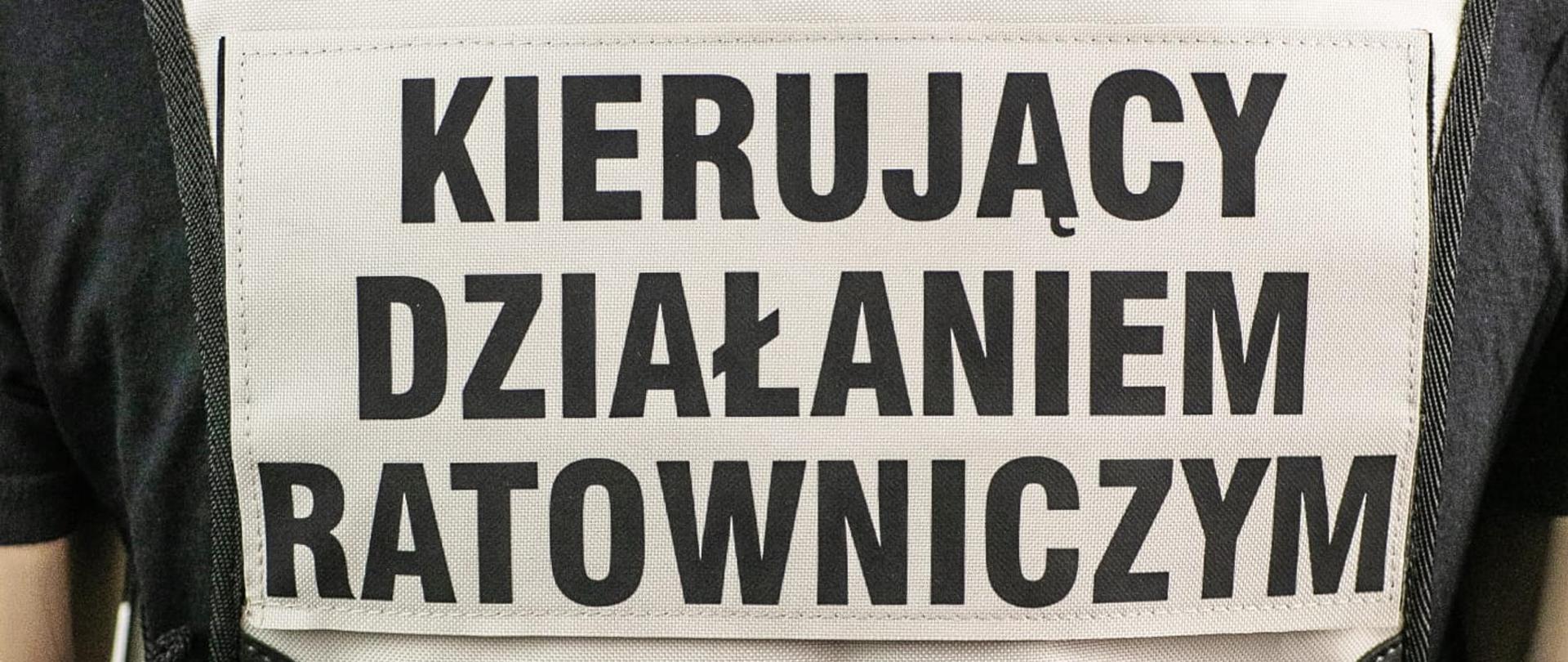Kamizelka w kolorze białym z czarnym napisem o treści Kierujący działaniem ratowniczym.