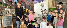 Grupa dzieci wraz z opiekunem i inspektorem pozuje do wspólnego zdjęcia w bibliotece podczas akcji „Drzewko dla Ziemi” 