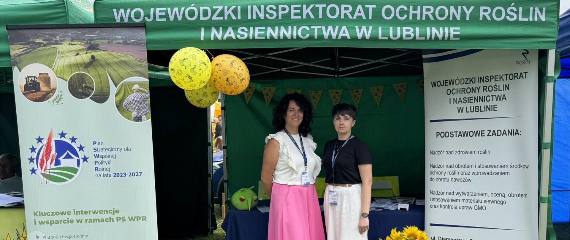 Pracownicy Wojewódzkiego Inspektoratu Ochrony Roślin i Nasiennictwa w Lublinie na stoisku podczas wydarzenia XXI Dzień Pszczelarza w Hańsku stoją na tle namiotu i stojaków reklamowych