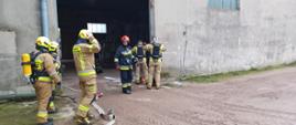 Pożar w budynku magazynowym. Na pierwszym planie widać rotę wchodzącą do magazynu z linią gaśniczą oraz rotę zabezpieczającą pracę roty w aparatach ochrony układu oddechowego działającej wewnątrz budynku i kierującego działaniem ratowniczym.