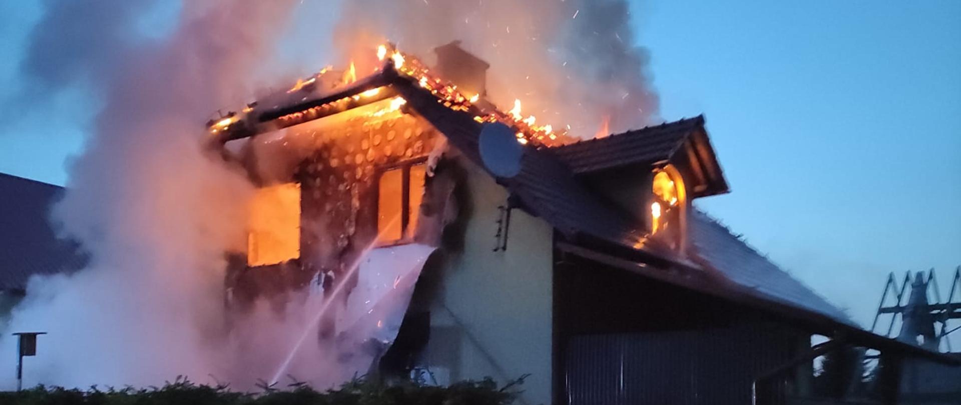 Na zdjęciu poddasze budynku mieszkalnego objęte pożarem. Widoczne płomienie wydobywające się z budynku