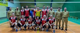 Strażacy, zawodnicy zwycięskiej drużyny pozują do zdjęcia razem z komendantami na boisku hali sportowej.