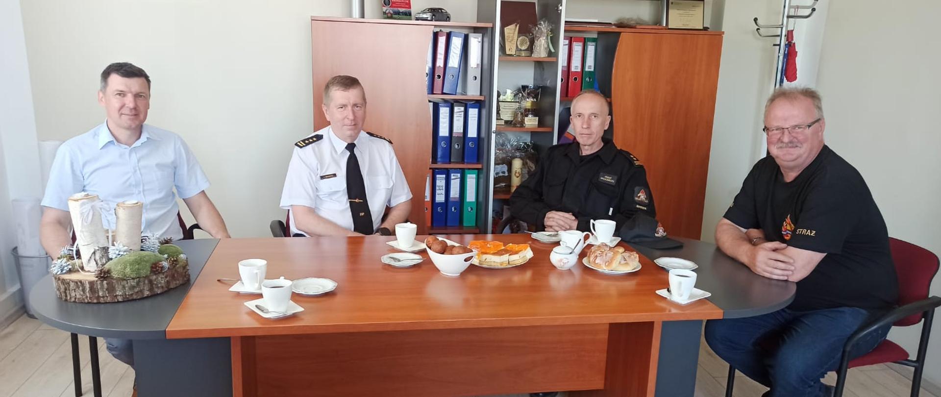 Zdjęcie przedstawia 4 mężczyzn siedzących przy stole podczas uzgodnień, dwóch z nich jest w mundurach.