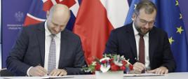 Minister funduszy i polityki regionalnej Grzegorz Puda siedzi przy stole i podpisuje porozumienie o współpracy w obszarze polityki spójności między Polską a Słowacją, po jego lewej stronie siedzi minister inwestycji, rozwoju regionalnego i informatyzacji Republiki Słowackiej Peter Balík i też podpisuje dokument porozumienia