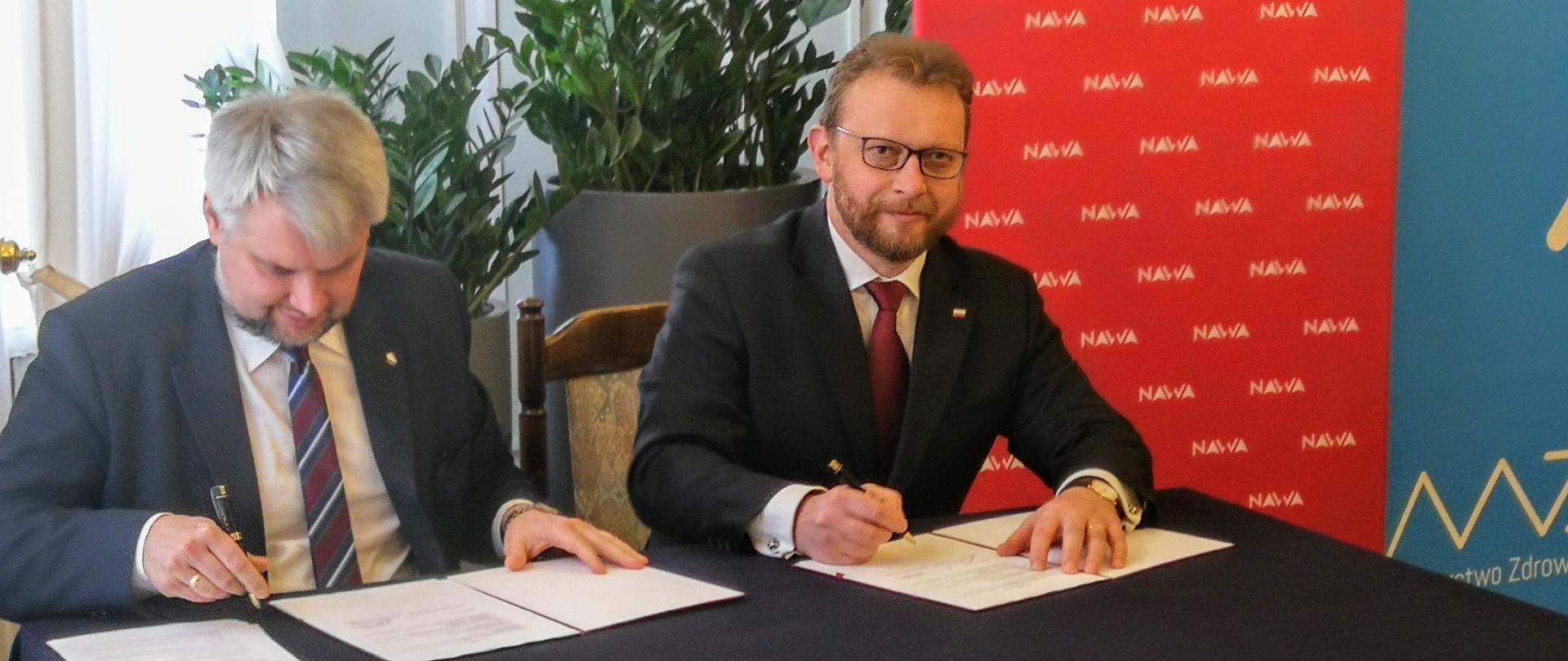 Minister Zdrowia Łukasz Szumowski i dyrektor Narodowej Agencji Wymiany akademickiej Łukasz Wojdyga podpisują umowę na obsługę i realizację programu NAWA im. prof. Walczaka "Wsparcie Mobilności Naukowców".