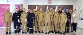 Pamiątkowe zdjęcie grupowe funkcjonariuszy PSP będących uczestnikami szkolenia „Prąd elektryczny, a zagrożenia dla strażaków” (14 osób) w towarzystwie Zastępcy Komendanta Centralnej Szkoły PSP, kobiety oraz dwóch funkcjonariuszy CS PSP