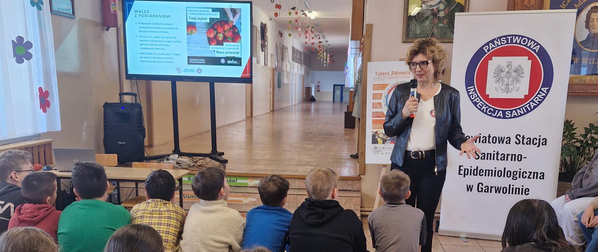 Pogadanka z młodzieżą. W tle pokaz slajdów i baner z logo Państwowej Inspekcji Sanitarnej.