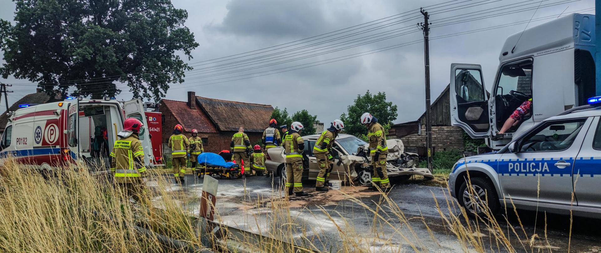 Droga, karetka pogotowia, rozbity samochód osobowy, radiowóz policyjny, dookoła strażacy
