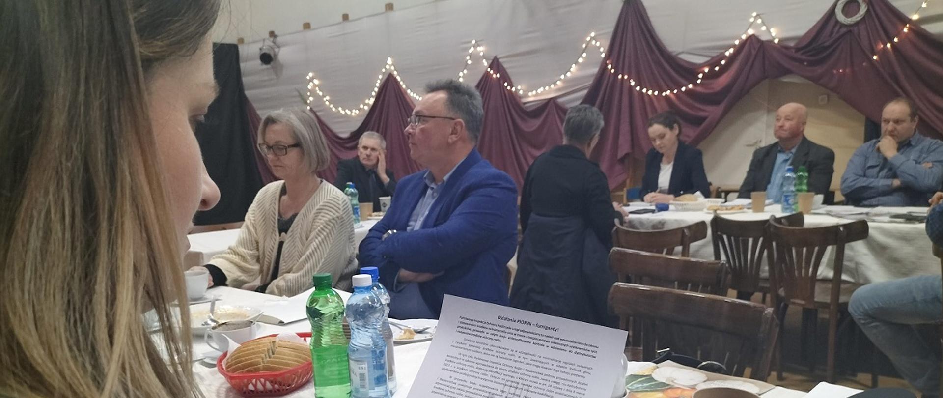 Osoba czyta ulotkę na spotkaniu. Uczestnicy siedzą w udekorowanej sali