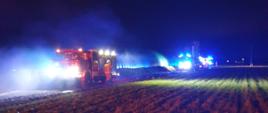 Zdjęcie w porze nocnej. Widać samochody ratowniczo-gaśnicze oraz budynek kurnika. Występuje zadymienie.