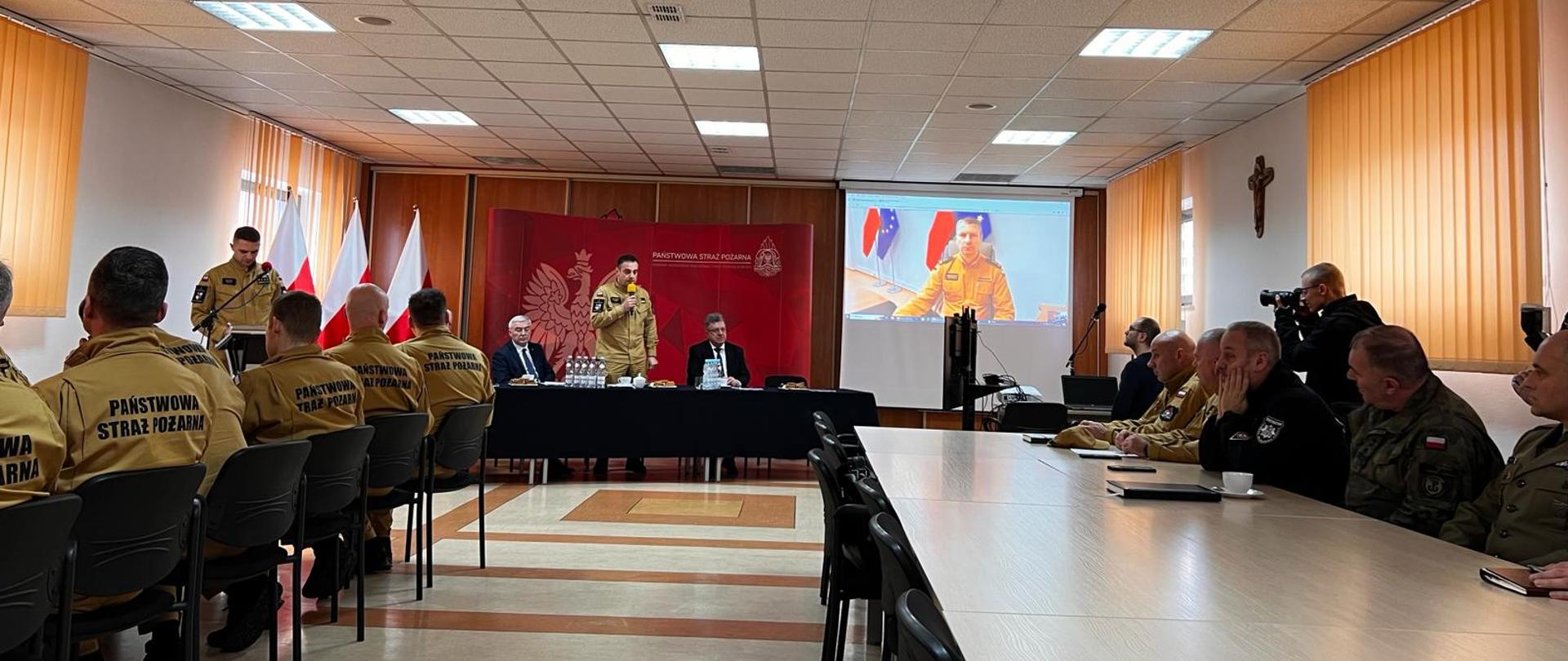 Na zdjęciu widzimy uczestników narady za stołami podczas dyskusji. Na zdjęciu przemawia ŚKW PSP