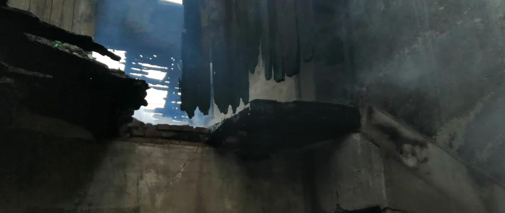 Zdjęcie przedstawia widok wnętrza budynku po pożarze. Uwidoczniony jest przepalony strop oraz dach.