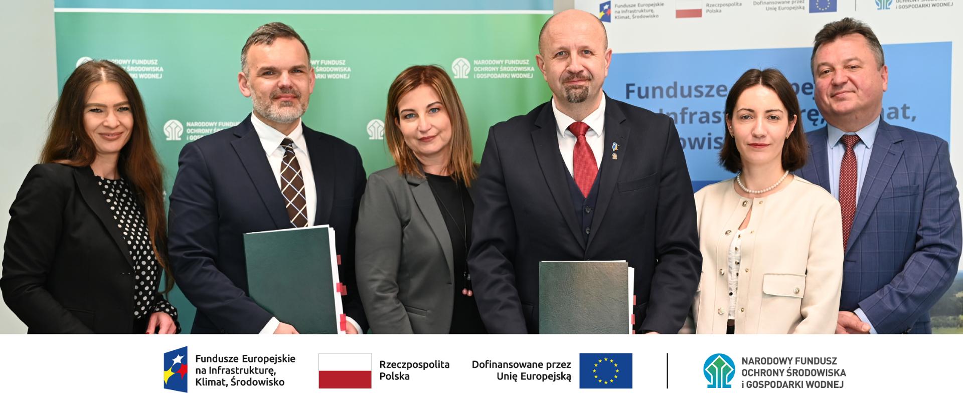 Zdjęcie grupowe. W stopce grafiki ciąg logotypów: Fundusze Europejskie na Infrastrukturę, Klimat, Środowisko, flaga Rzeczypospolita Polska, flaga UE i Dofinansowane przez UE, NFOŚiGW.