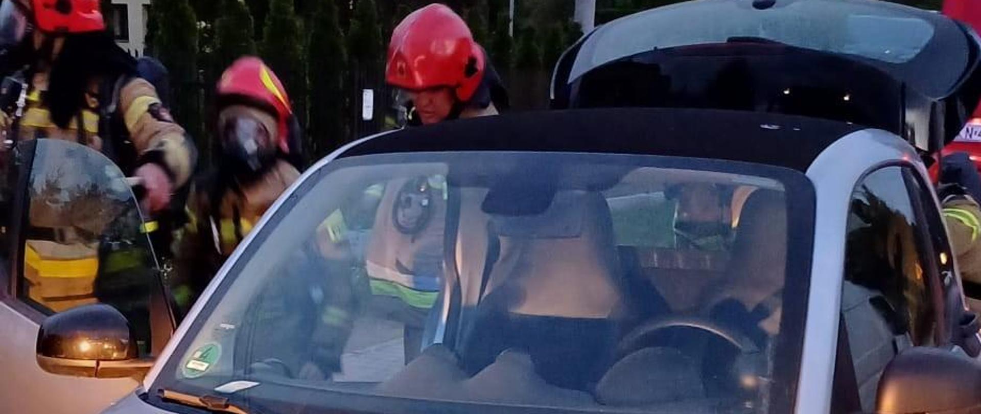 Samochód elektryczny a obok strażacy