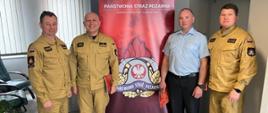 Grupowe zdjęcie wyróżnionych strażaków oraz komendanta i jego zastępcy. Na drugim planie baner komendy powiatowej.