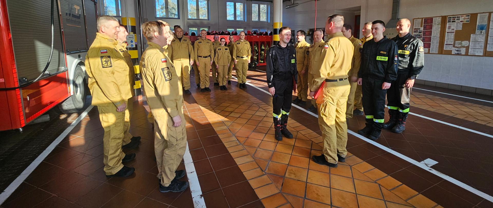 Strażacy stoją w szyku w garażu, komendant wręcza decyzję