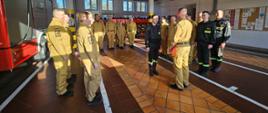 Strażacy stoją w szyku w garażu, komendant wręcza decyzję